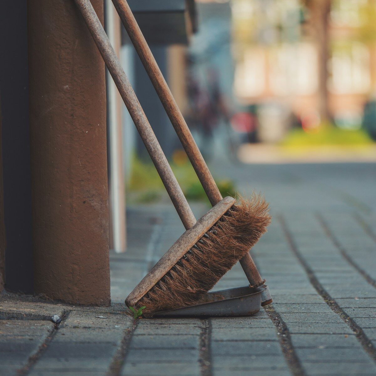 a broom leaning against a pole on a sidewalk